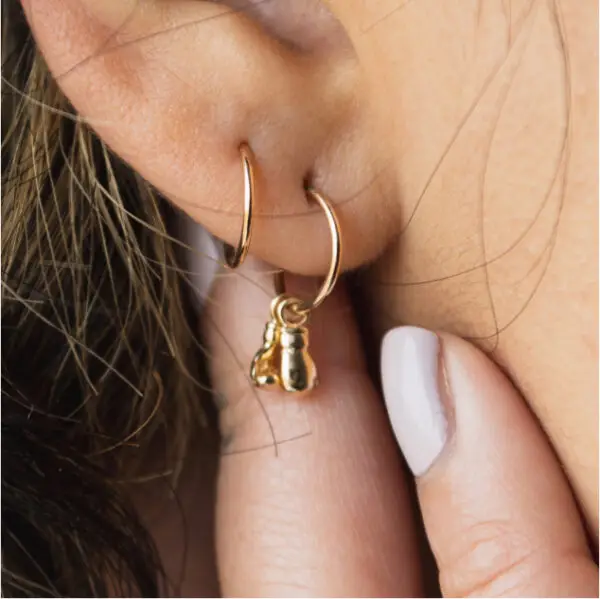 A woman wearing gold earrings and white nails.