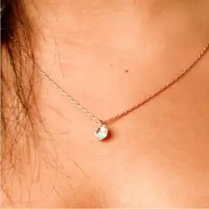 A woman wearing a necklace with a small diamond on it.
