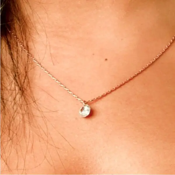 A woman wearing a necklace with a small diamond on it.
