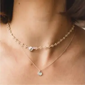 A woman wearing two necklaces on her neck.