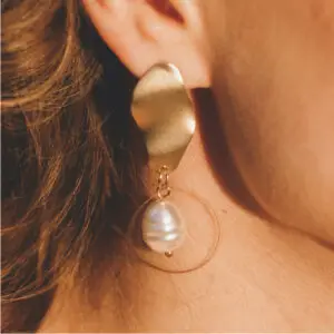 A woman wearing gold earrings with a pearl hanging from the bottom of her ear.