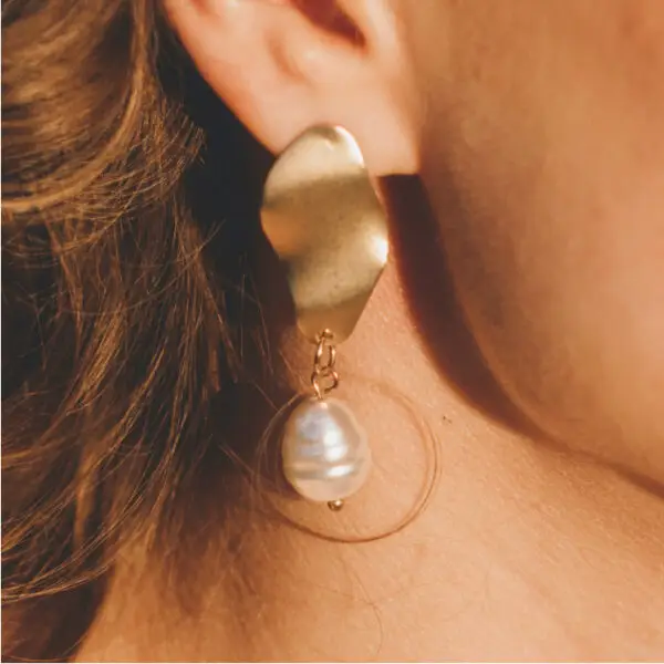 A woman wearing gold earrings with a pearl hanging from the bottom of her ear.