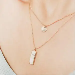 A woman wearing two necklaces on her neck.