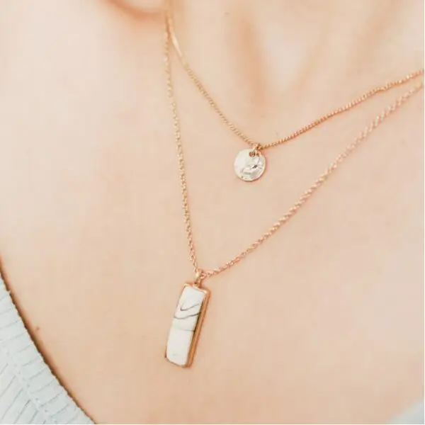 A woman wearing two necklaces on her neck.