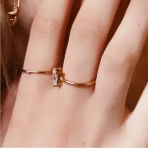 A woman wearing a gold ring with an emerald cut diamond.