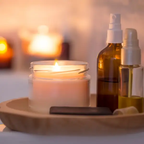 A candle, candles and some bottles of lotion on a tray.