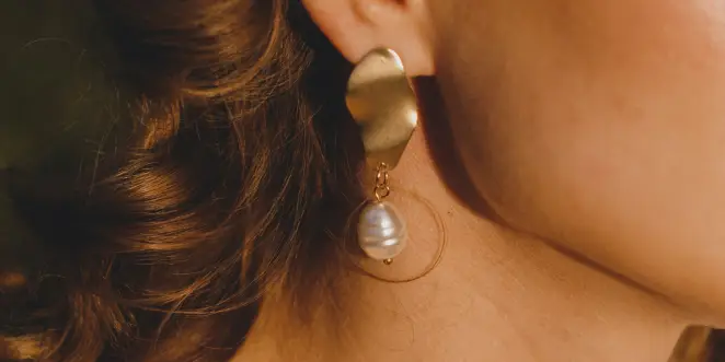 A woman wearing large gold earrings with pearls.
