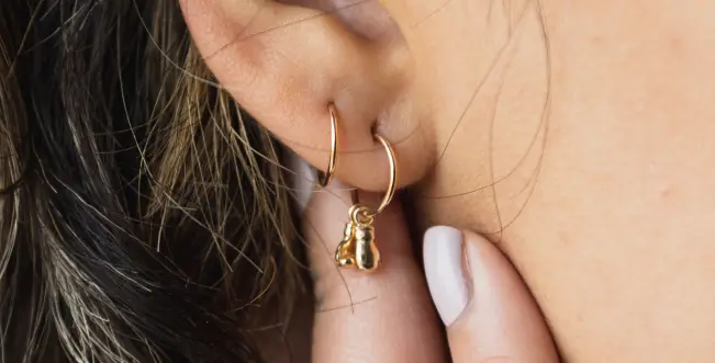 A woman 's ear with two small gold earrings hanging from it.