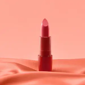 A red lipstick is sitting on top of the pink cloth.